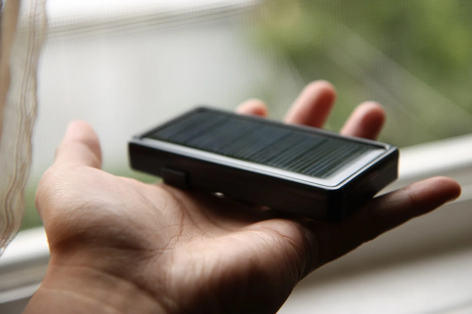 Mano sujetando una batería externa con un pequeño panel solar integrado