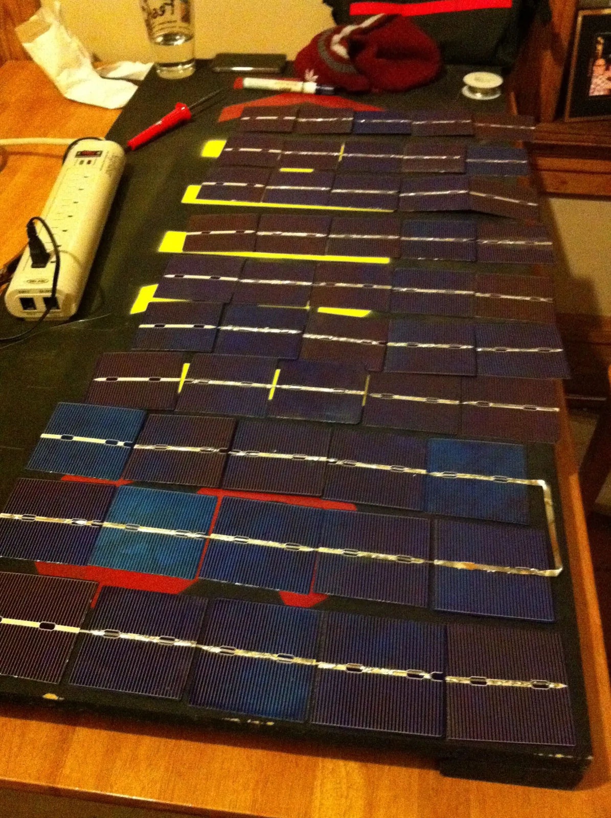 Células solares unidas con cinta de conexión y colocadas en filas sobre una mesa para montar un panel casero