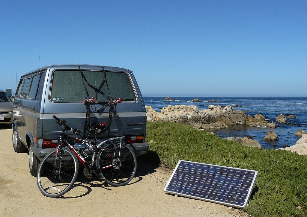 Panel solar portátil junto a una furgoneta camper en un viaje por la costa